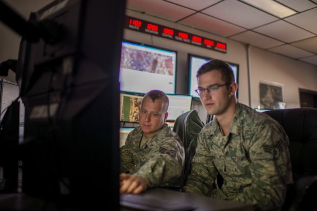 Two airmen focus on a computer screen.