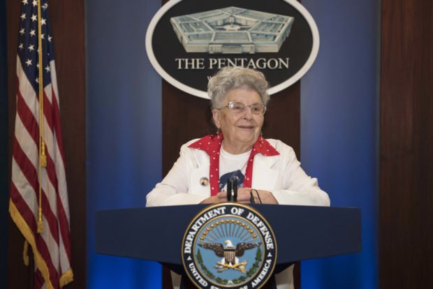 A woman stands at a lectern with the DOD logo.