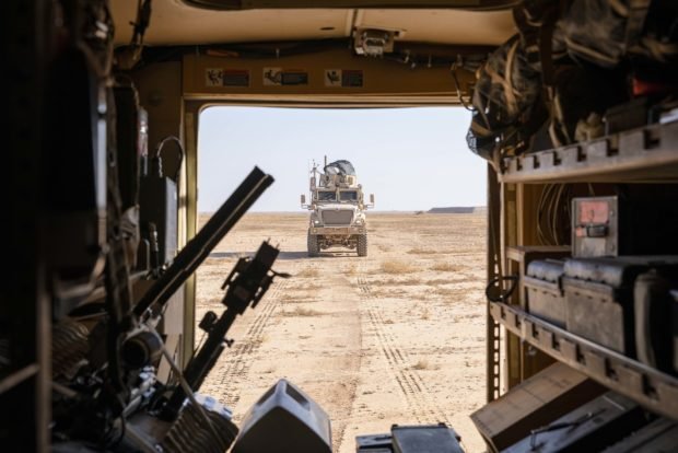 A military vehicle drives through dirt.