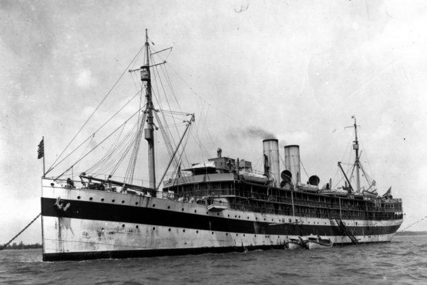 Black-and-white image of a large ship at anchor.