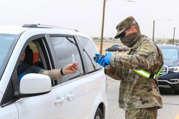 A soldier wearing personal protective equipment checks a motorist’s ID card at an entry control point.