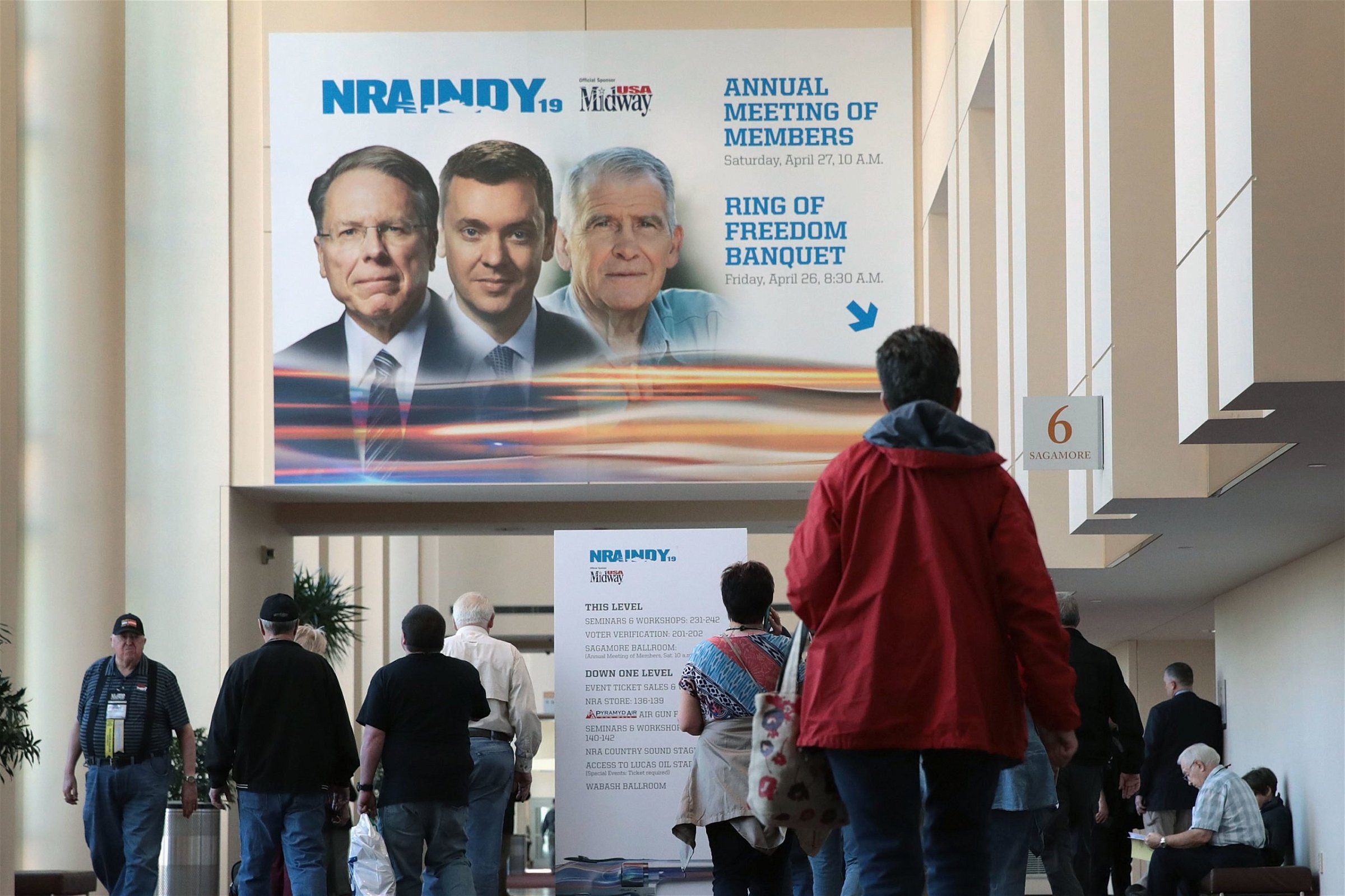 INDIANAPOLIS, INDIANA - APRIL 27: Guest walk under a poster featuring Wayne LaPierre (L), NRA vice president and CEO, Chris Cox (C), executive director of the NRA-ILA, and NRA president Oliver North outside a conference room where the NRA annual meeting of members was being held at the 148th NRA Annual Meetings & Exhibits on April 27, 2019 in Indianapolis, Indiana. A statement was read at the meeting announcing that NRA president Oliver North, whose seat at the head table remained empty at the event, would not serve another term. There have been recent reports of tension between LaPierre and North, with North citing financial impropriety within the organization. (Scott Olson/Getty Images)