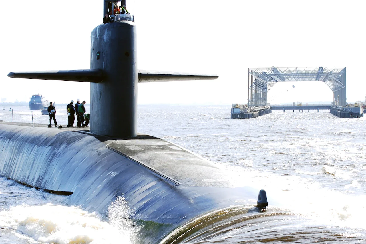 Six submariners stand atop of a submarine as it returns to its home port.
