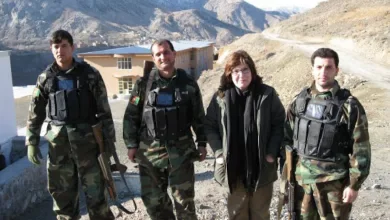A woman and three men pose for a photo in rough terrain; mountains are in the background.